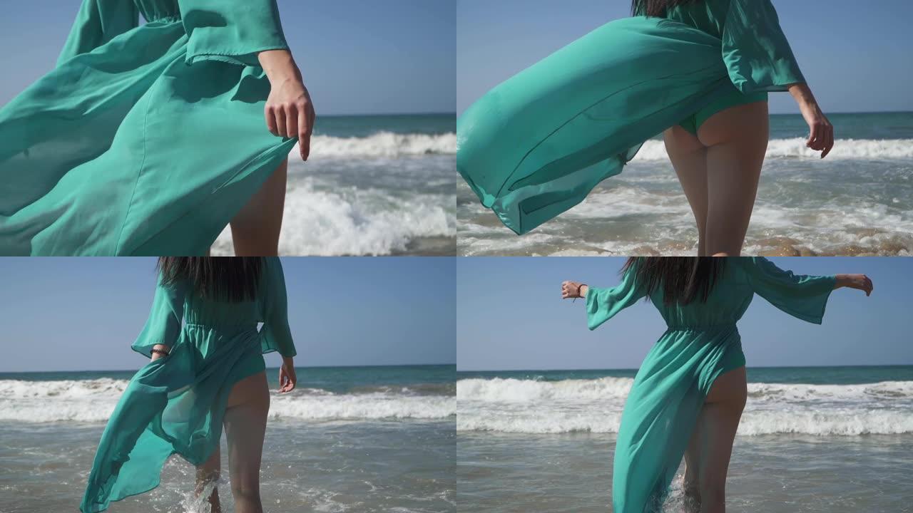 身材完美的女人穿着绿松石色的裙子走进了大海。裙子在风中飘动，浪花拍打着美丽的女性双腿。