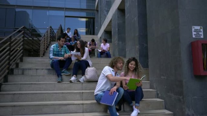 大学里的学生们坐在楼梯上分组或情侣学习