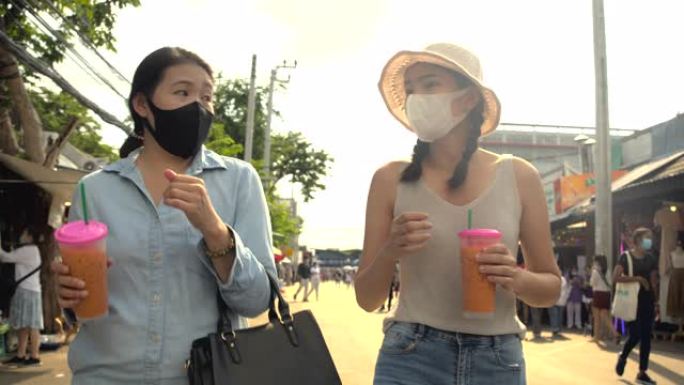 两名亚洲妇女一起走出当地市场。戴口罩。