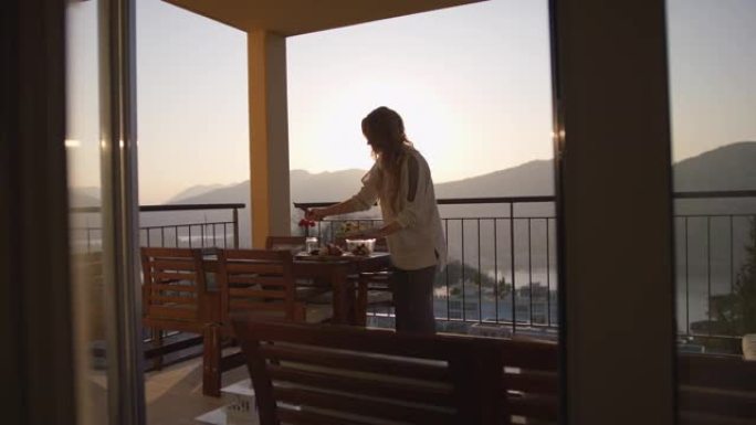 公寓阳台上的女人在后面准备饭菜、山脉和日落