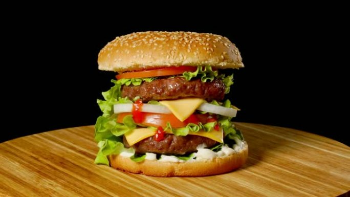 伟大的汉堡，牛肉排，西红柿，蘑菇和黄瓜，融化的奶酪在黑色背景上的木板上旋转