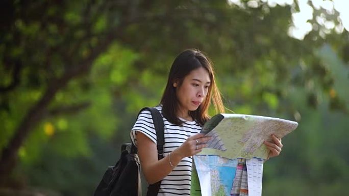 背着背包的年轻女子在海滩上欣赏风景，看着地图。