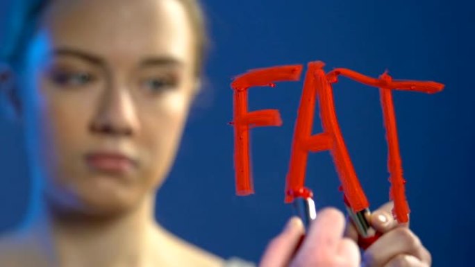 不安全的少女在镜子上用口红写丑陋的单词，厌食症问题
