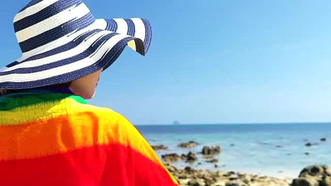 热带暑假时尚概念 -- 年轻女性，戴着彩色围巾站在海滩上。