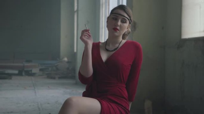 画像中优雅的女子穿着红色优雅的连衣裙坐在废弃大楼的椅子上抽烟。