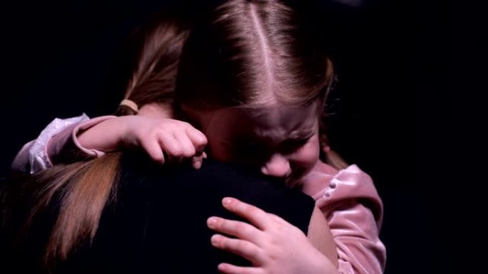 受惊的女孩拥抱母亲并在黑色背景下哭泣