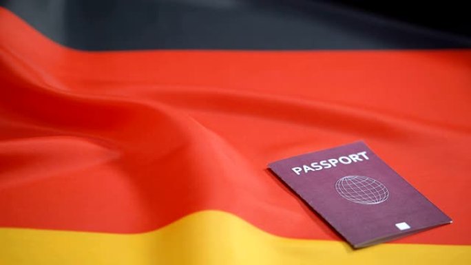 女性手将国际红色护照放在德国国旗上，旅行证件