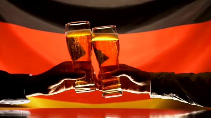男人叮当作响的啤酒杯，背景上的德国国旗，庆祝节日