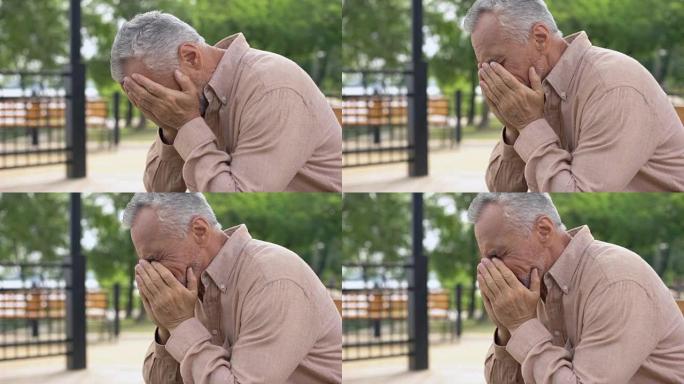 悲伤的老人坐在医院花园的长凳上，退休人员在悲伤中哭泣