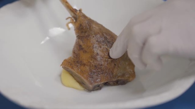 库克的双手戴着白色橡胶手套，将肋骨和肉放在盘子上融化的奶酪上。