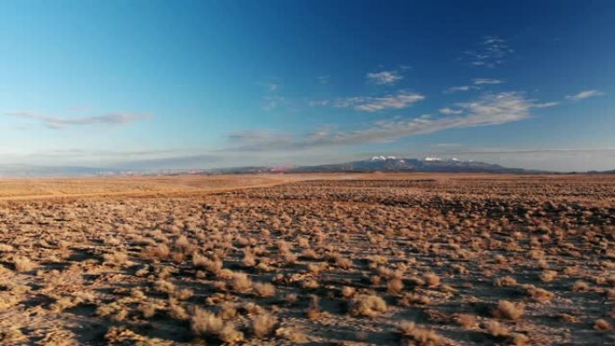 移动无人机拍摄的沙漠平原，背景是犹他州摩押外的山脉，日落/日出时在蓝天下