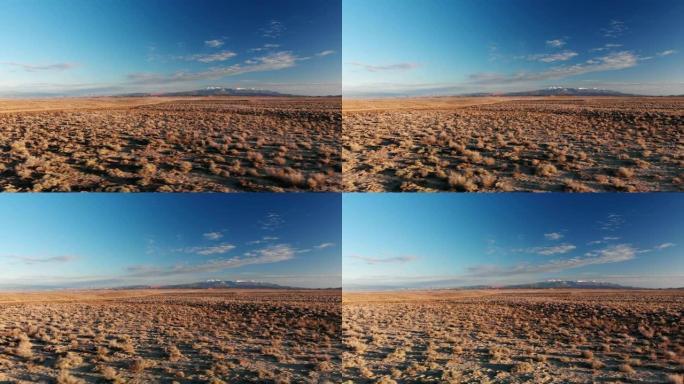 移动无人机拍摄的沙漠平原，背景是犹他州摩押外的山脉，日落/日出时在蓝天下
