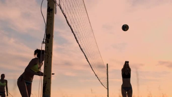 穿着比基尼的性感排球女孩在沙滩上玩夏季排球日落时在沙滩上慢动作。