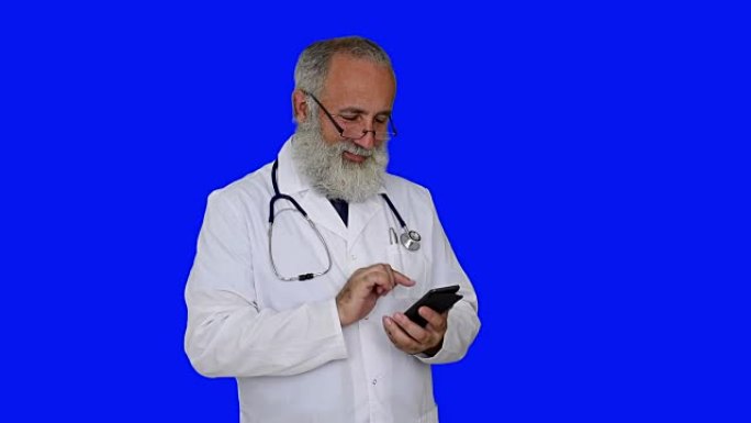 成人高级医生微笑并在蓝色背景上使用智能手机