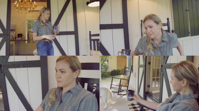 慢动作拍摄了一个四十多岁的白人妇女走出艺术工作室的双谷仓门，坐在门廊摇椅上，喝杯咖啡和她的狗，欣赏户