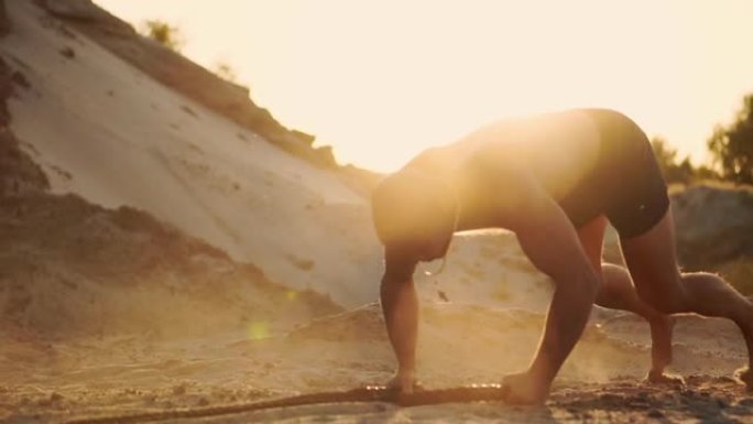 男运动员在沙滩上做俯卧撑，拍打地面上的绳子，在阳光下循环训练，在沙滩上以慢动作扬起尘土