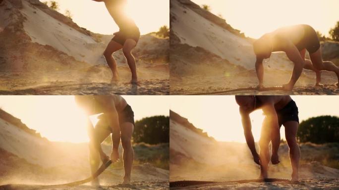 男运动员在沙滩上做俯卧撑，拍打地面上的绳子，在阳光下循环训练，在沙滩上以慢动作扬起尘土