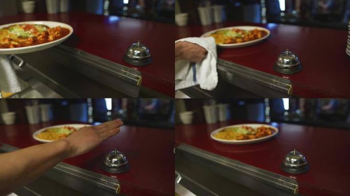 一个人拿起一盘墨西哥热食物，将其放在服务窗口中，并在一家墨西哥餐厅为服务员敲响钟