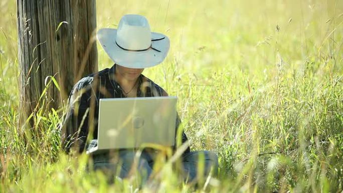 牛仔使用笔记本电脑坐在草地上