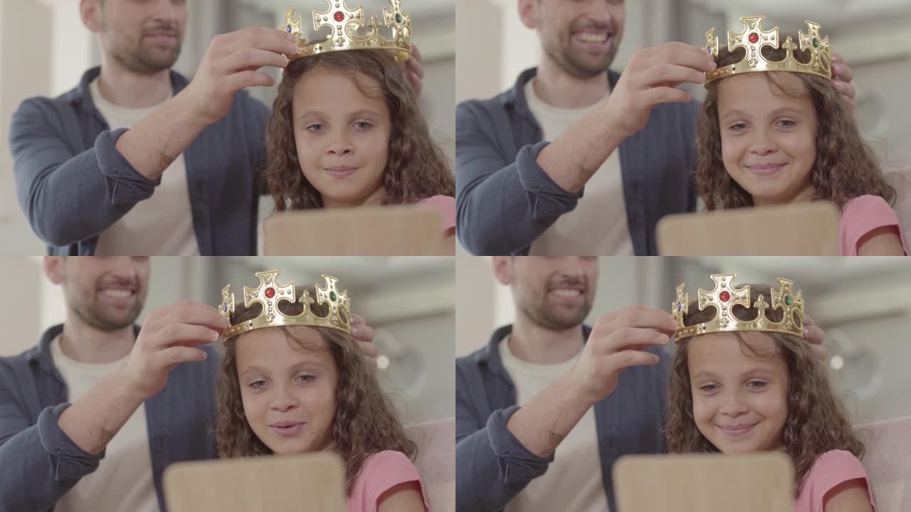 肖像父亲把皇冠戴在照镜子的卷发女孩的头上。