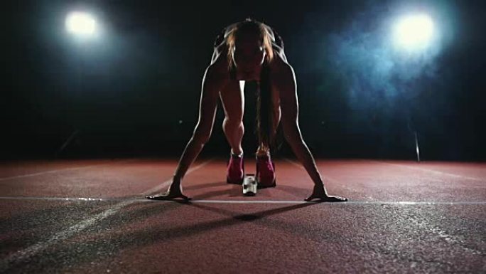 职业女运动员在黑暗的背景下，在体育场的跑道上，在黑暗的背景下，穿着运动鞋跑慢跑鞋的冲刺。特写