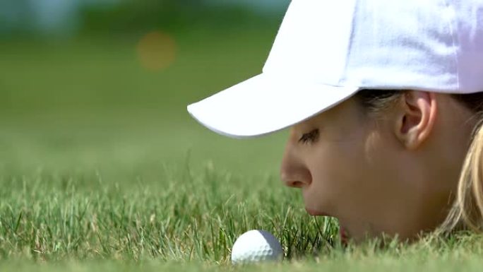 女子高尔夫初学者躺在草地上，把球吹进洞里，玩得开心