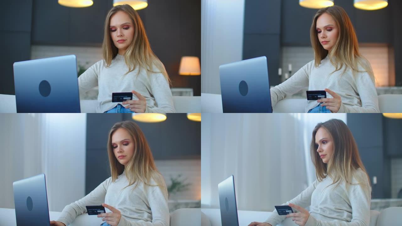 一个漂亮的金发女郎坐在沙发上，拿着笔记本电脑和信用卡在网上银行研究她的信用记录