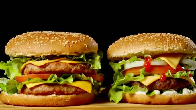两个开胃汉堡的特写镜头，芝麻面包在黑色背景上旋转，快餐无缝循环拍摄