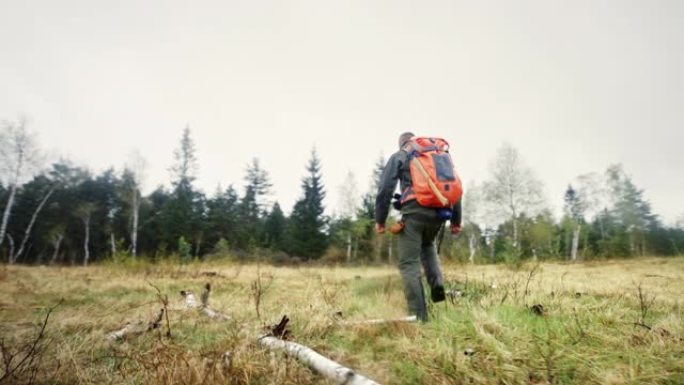 一名男子醒来穿过一大片森林空地，背着一个大背包