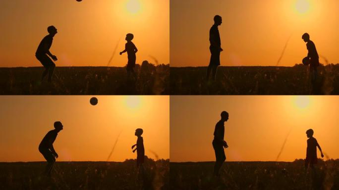 父亲和儿子在日落时在公园踢足球，在灿烂的阳光，慢动作拍摄的背景下剪影