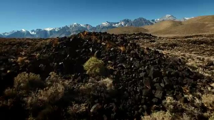 低空飞行的无人机在岩石和陆地上射击，在晨曦中露出雪顶山脉。