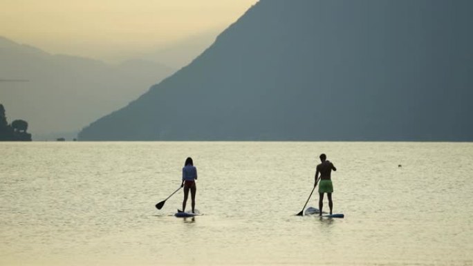 年轻夫妇在日出时站在湖上划板