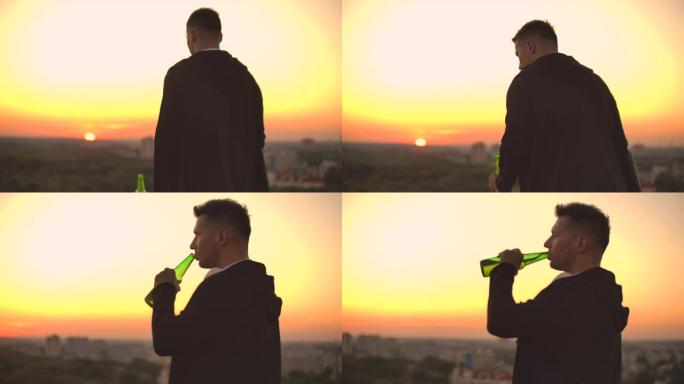 从后面看，一个男人在日落时走在屋顶上，喝啤酒，看着城市的美丽景色