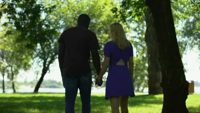 跨种族夫妇牵手在公园散步的背景图，关系