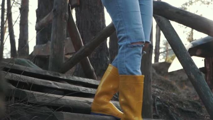穿着黄色胶靴的人腿在森林的木制楼梯上走下。穿着橡胶靴的脚从户外的木制楼梯下来。
