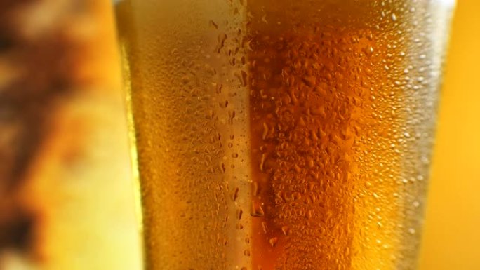 在带有橙色液体的玻璃杯中升起的细气泡的宏观镜头。装有水滴的玻璃杯中的冷淡啤酒。精酿啤酒特写。旋转36