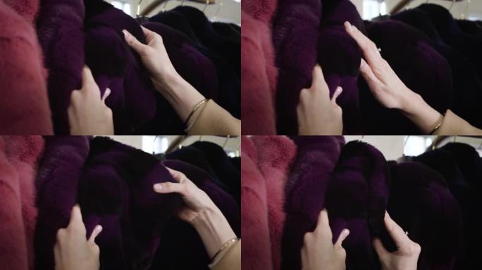 年轻的女性高加索人的手在商店里触摸紫罗兰皮大衣的特写镜头。富有时尚的女人在精品店购物。生活方式、时尚