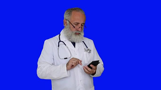 成人高级医生在蓝色背景上使用智能手机