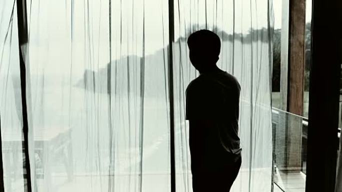 一个年轻人站在窗户旁用手机聊天的特写镜头