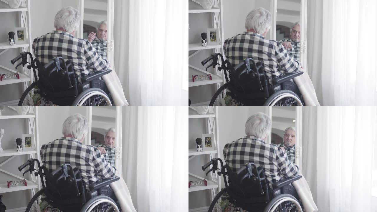 坐在轮椅上的成熟高加索人看着镜子里的倒影的特写镜头。悲伤的老年退休人员独自在室内度过一天。记忆，衰老