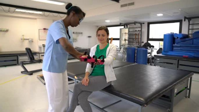 女性黑人治疗师帮助女性患者在进行物理治疗后戴上手托
