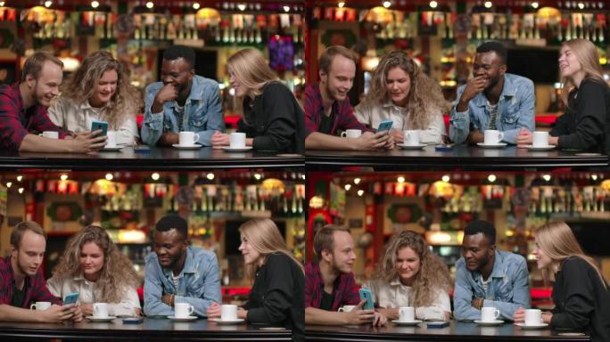 非裔美国男子和一个女孩看着智能手机，一边坐在咖啡里喝咖啡一边聊天，朋友一群人在餐馆里