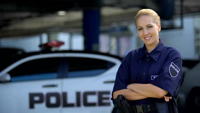女警官微笑着，双手交叉站在巡逻车附近，法律