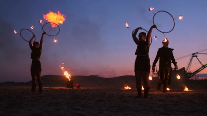 火秀三个女人在他们的手扭动燃烧的长矛和风扇在沙子与一个男人两个喷火器在慢动作。