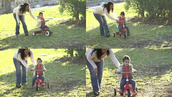 母亲帮助小男孩骑三轮车
