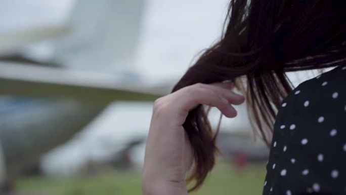女性的手在模糊的飞机前触摸她的黑发的特写。
