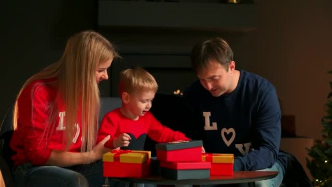 爸爸妈妈和儿子在圣诞节打开礼物在家坐在圣诞节室内的沙发上。温暖舒适的家庭氛围