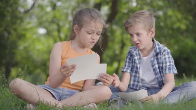 穿着方格衬衫的可爱英俊男孩和长发女孩在公园里看着纸的肖像。