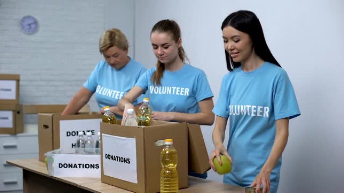 穿着志愿者t恤的快乐妇女放罐头食品盒，捐赠