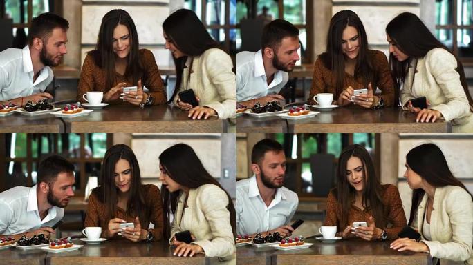 开朗的青少年潮男一边看着相机，一边用智能手机向女友展示视频，恋爱中的浪漫情侣一起在咖啡馆露台上观看手